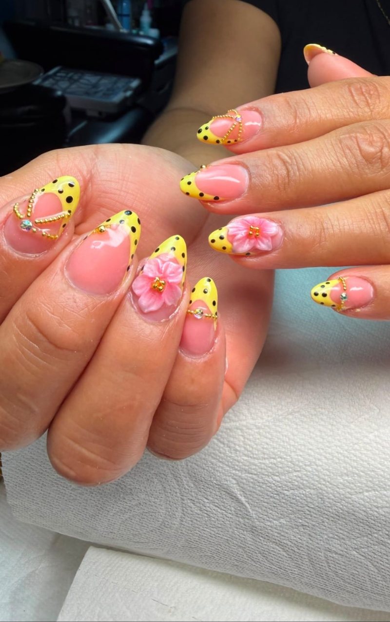 Uñas amarillas con lunares negros, flor 3D rosa y pedrería dorada